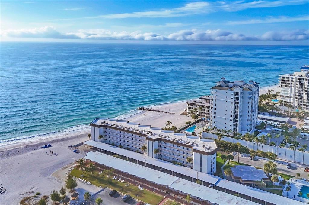 An aerial view shows beachfront hotel buildings with a swimming pool and sandy shoreline — 2110 BENJAMIN FRANKLIN DRIVE UNIT 104, SARASOTA, FL