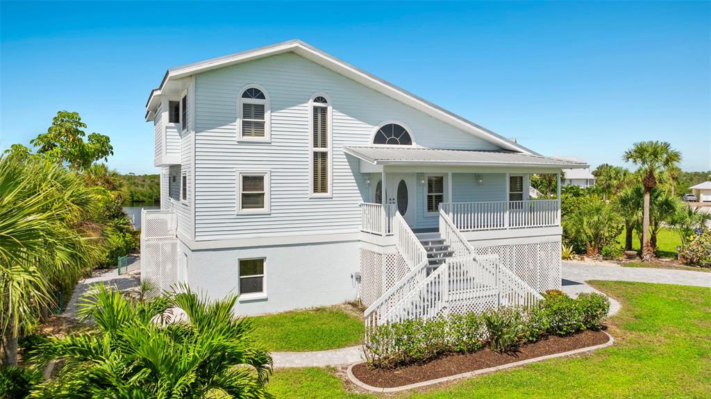 A light blue, elevated two-story house features a front porch, stairs, and surrounding landscaping — 13065 VIA AURELIA, PLACIDA, FL