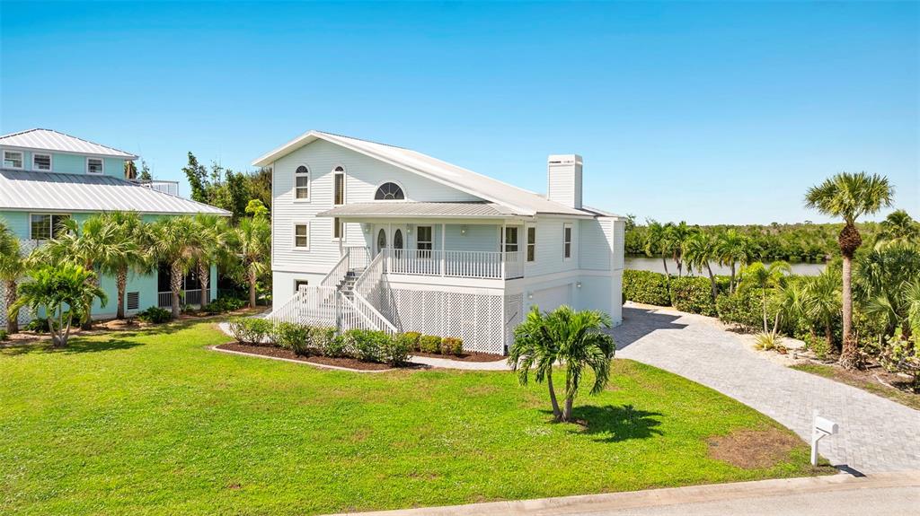 A light blue, elevated two-story house with a metal roof and a paved driveway — 13065 VIA AURELIA, PLACIDA, FL