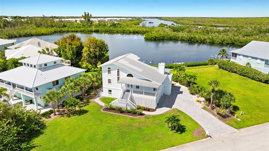 An aerial view shows two elevated houses with metal roofs situated near a waterfront — 13065 VIA AURELIA, PLACIDA, FL