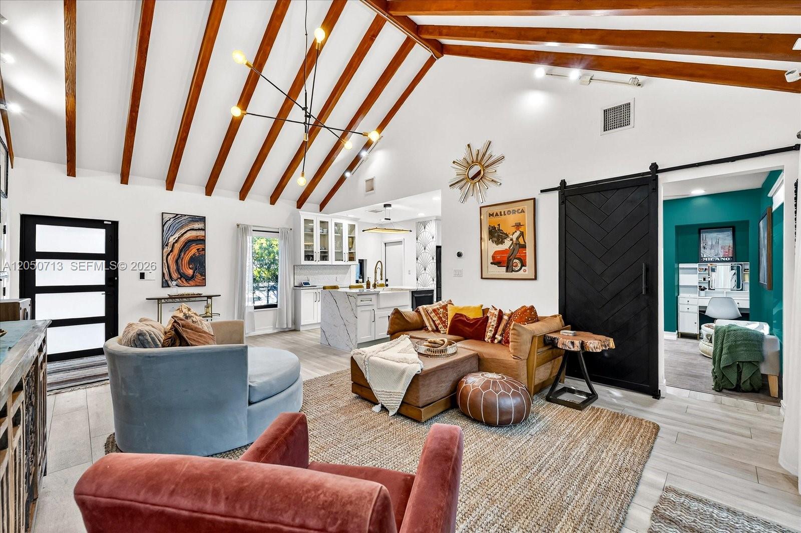 A living room with vaulted wood-beamed ceilings, a black barn door, and an open kitchen — 8225 NE 8th Ct, Miami FL 33138, MIAMI, FL