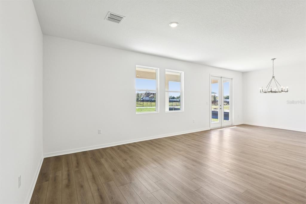 A bright, empty room features white walls, wood-look flooring, two windows, and glass patio doors — 1634 CANE BAMBOO DRIVE, ST CLOUD, FL