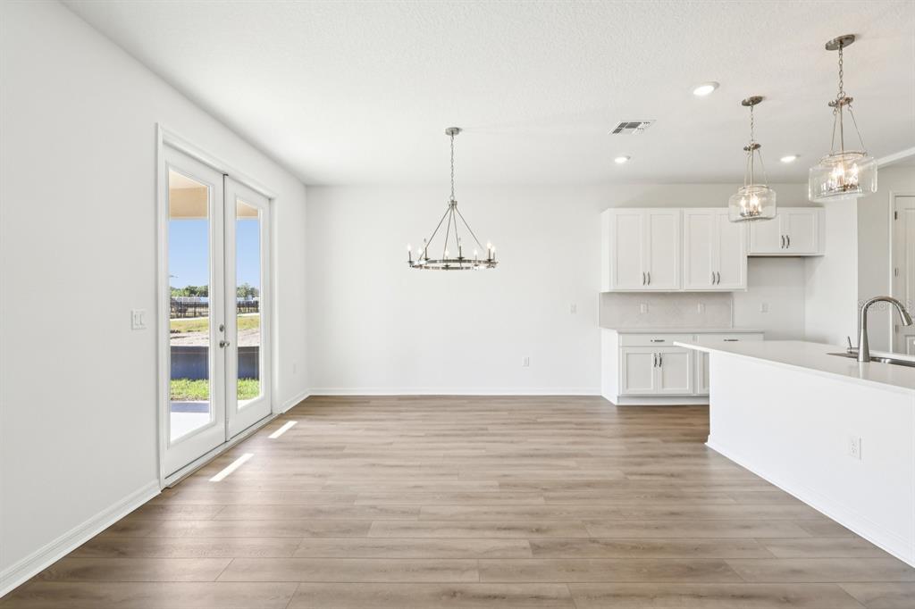 An open-concept dining area and kitchen with white cabinets, light wood flooring, and glass doors — 1634 CANE BAMBOO DRIVE, ST CLOUD, FL
