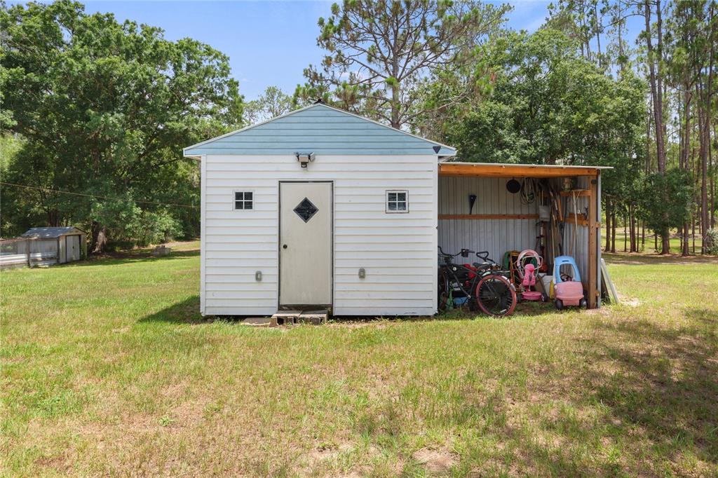 A white shed with a blue gable and an attached open-air storage area — 5360 DILLMAN LANE, POLK CITY, FL