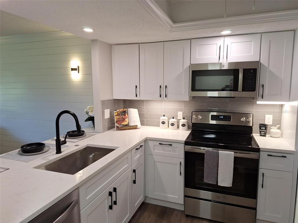 A modern kitchen features white cabinets, stainless steel appliances, quartz countertops, and a black faucet — 3700 BENEVA ROAD UNIT 0, SARASOTA, FL