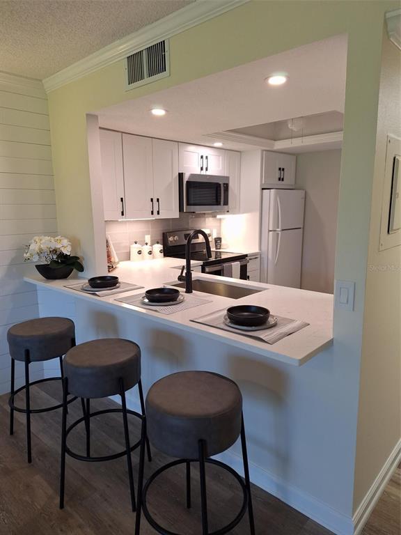 A kitchen with white cabinets, stainless steel appliances, and a breakfast bar with three stools — 3700 BENEVA ROAD UNIT 0, SARASOTA, FL