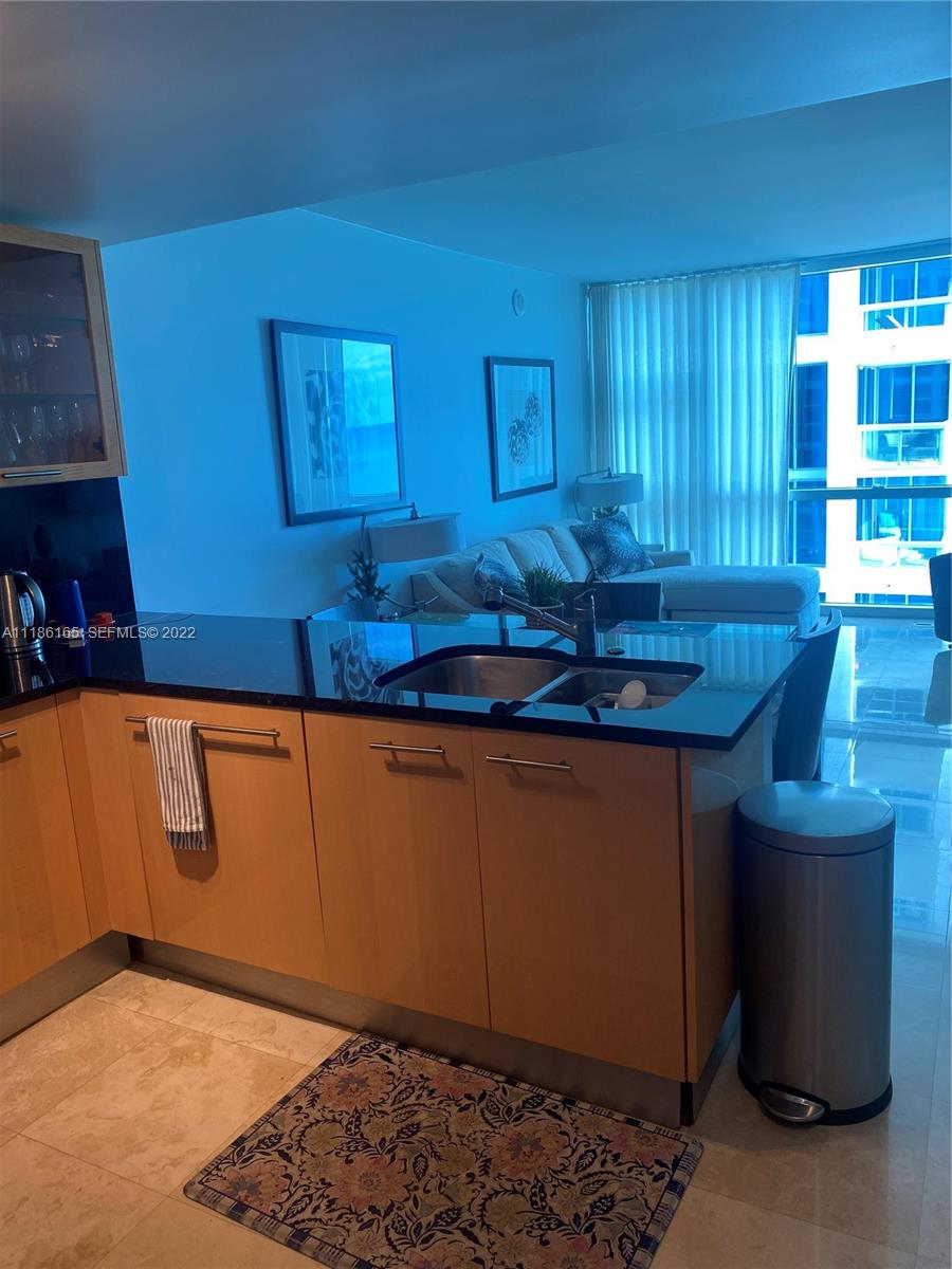 A kitchen with light wood cabinets and black countertops overlooks a living area with floor-to-ceiling windows — 6801 Collins Ave, Miami Beach FL 33141, MIAMI BEACH, FL