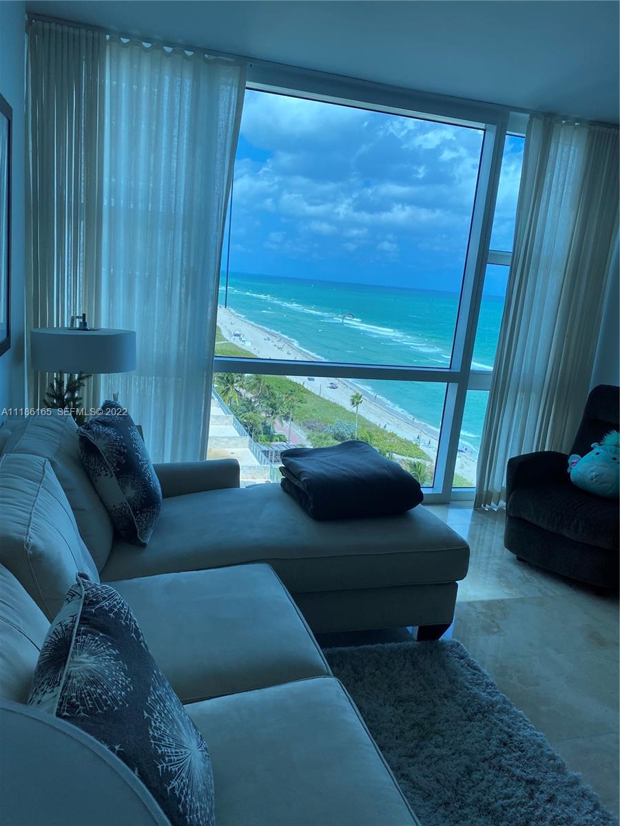 A living room features a light-colored sectional sofa and a large window overlooking the ocean — 6801 Collins Ave, Miami Beach FL 33141, MIAMI BEACH, FL