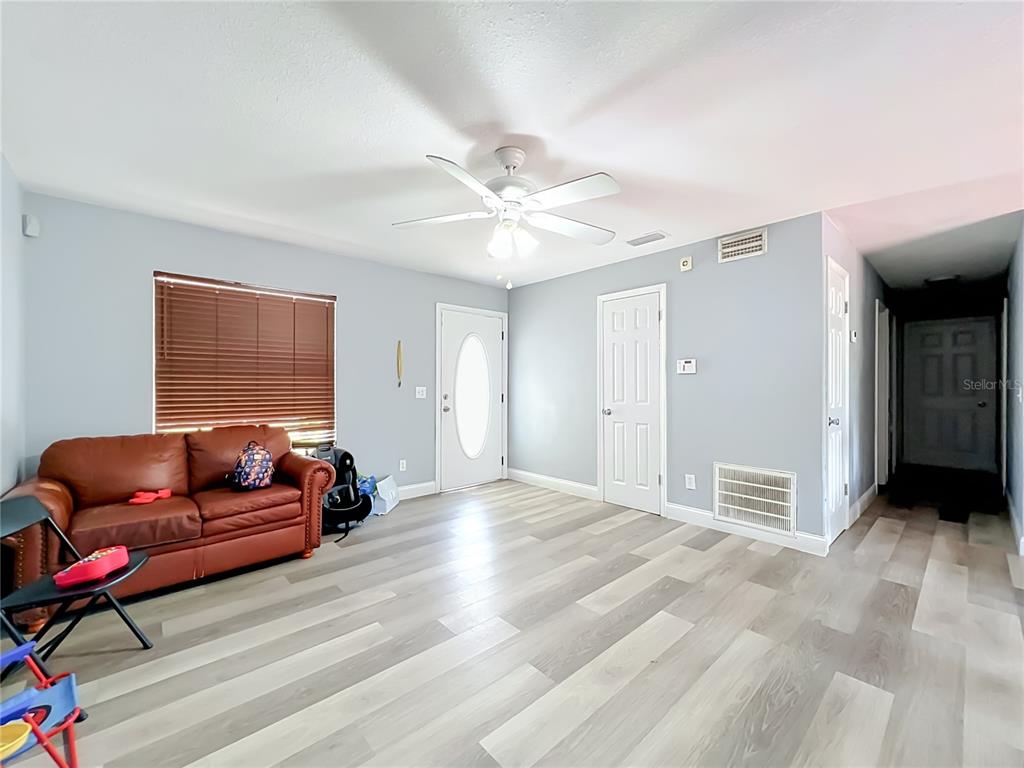 A living room features light gray walls, wood-look flooring, a ceiling fan, and a brown sofa — 5855 HUTTON DRIVE, ORLANDO, FL
