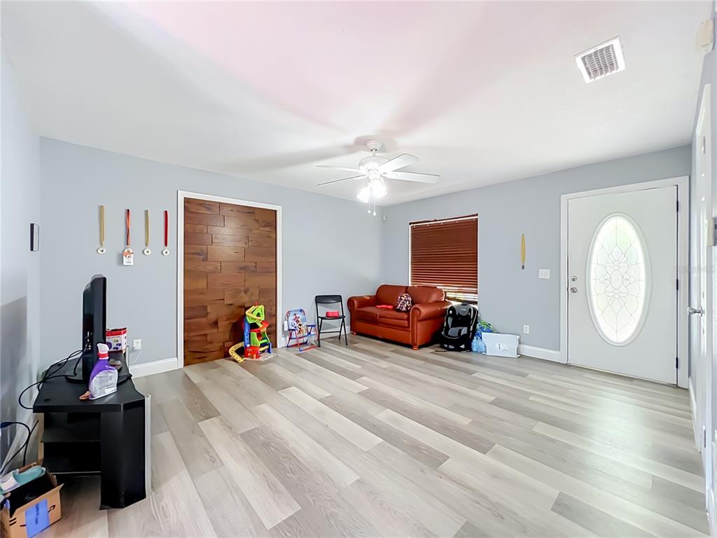 A living room features light-colored wood-look flooring, a wood-paneled accent wall, and a white front door — 5855 HUTTON DRIVE, ORLANDO, FL