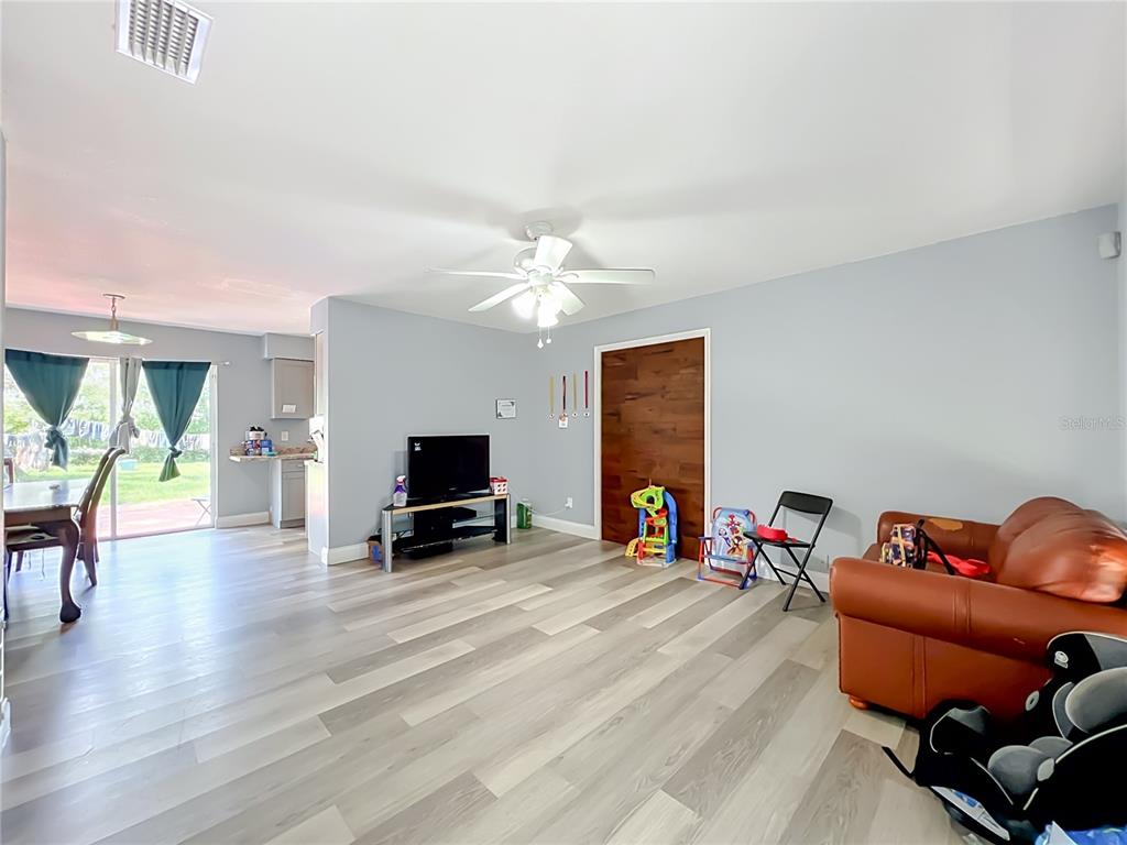 A living room with light wood-look flooring, a ceiling fan, and a dark wood door — 5855 HUTTON DRIVE, ORLANDO, FL