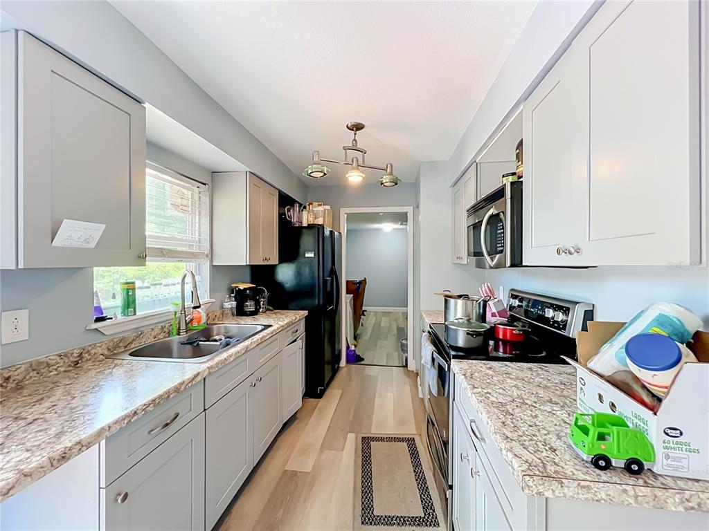 A galley kitchen features gray cabinets, marble-patterned countertops, stainless steel appliances, and light wood flooring — 5855 HUTTON DRIVE, ORLANDO, FL