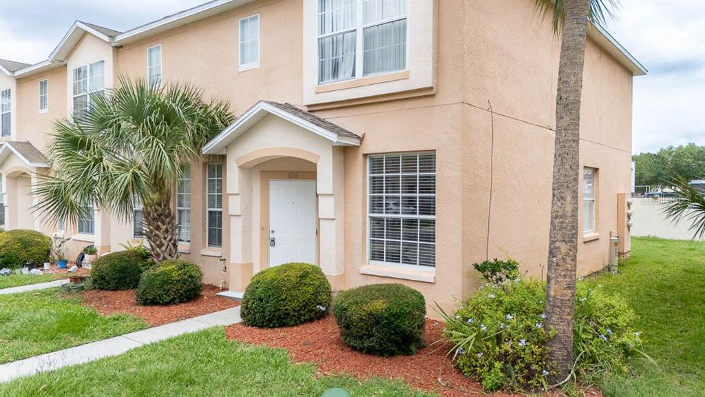 A two-story tan stucco townhouse features a covered entryway, palm trees, and manicured landscaping — 678 CAPTIVA CIRCLE, KISSIMMEE, FL