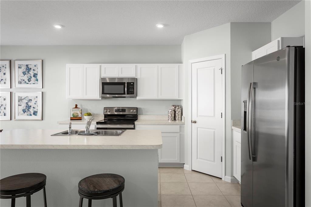 A kitchen features white cabinets, stainless steel appliances, a center island, and tile flooring — 1566 STARLING SONG LANE, LAKELAND, FL