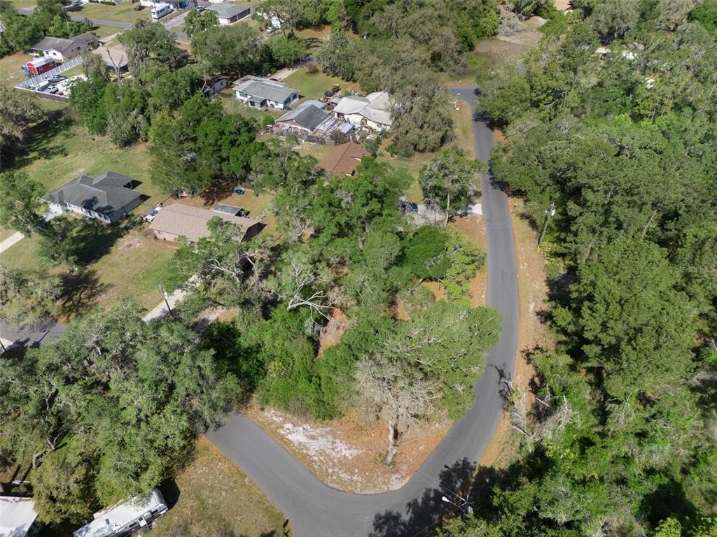 An aerial view shows a curved residential street surrounded by wooded lots and houses — 5043 CARDINAL DRIVE, DADE CITY, FL