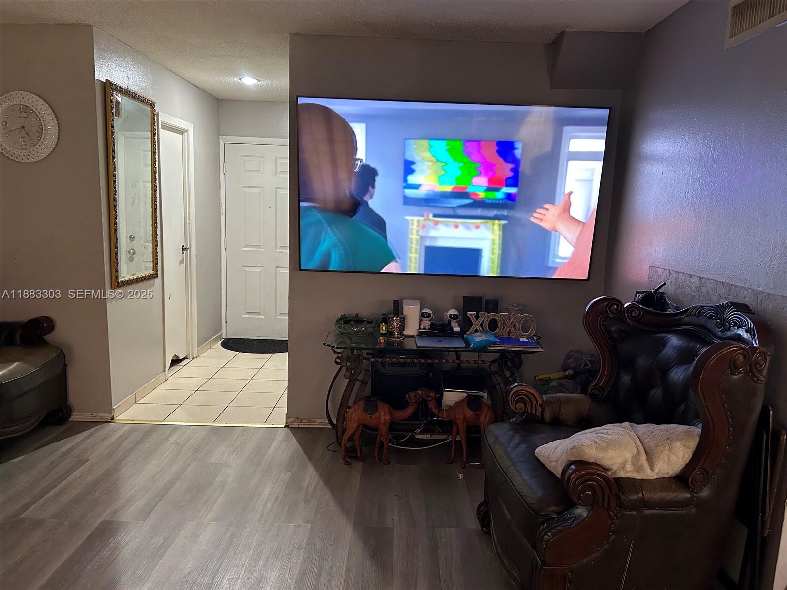 A living room features a wall-mounted television, a leather armchair, and a glass console table — 18111 NW 68th Ave # G206, Hialeah FL 33015, HIALEAH, FL