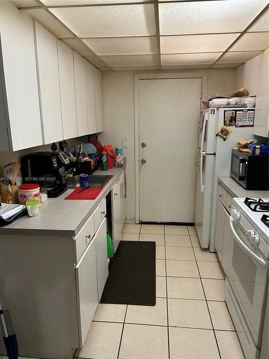 A galley-style kitchen features white cabinets, light countertops, a tiled floor, and a white door — 18111 NW 68th Ave # G206, Hialeah FL 33015, HIALEAH, FL