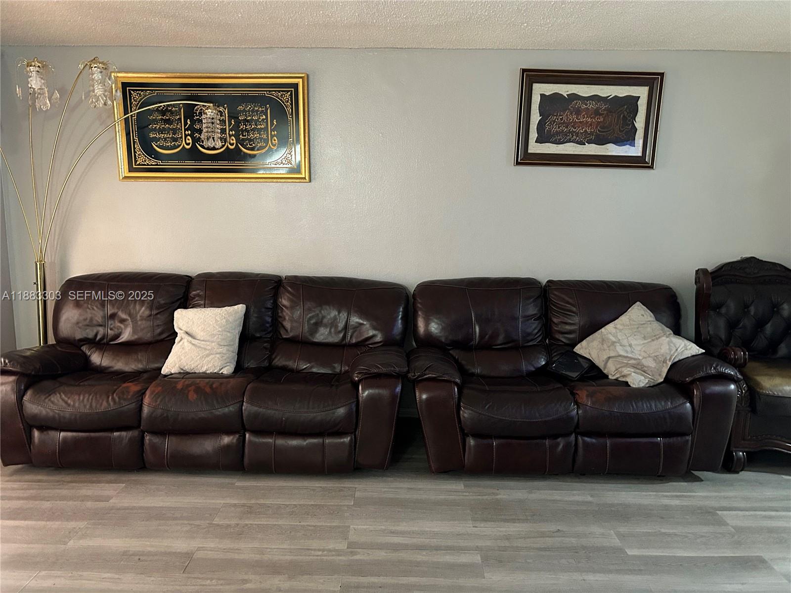 A living room features a dark brown leather sofa, two framed wall hangings, and a floor lamp — 18111 NW 68th Ave # G206, Hialeah FL 33015, HIALEAH, FL