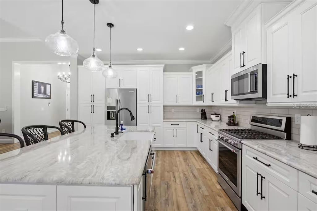 A modern kitchen features white cabinetry, a large marble-topped island, and stainless steel appliances — 9855 SW 125TH TERRACE, DUNNELLON, FL