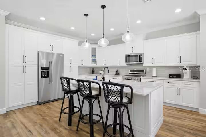 A modern white kitchen features a marble-topped island with three black wicker bar stools — 9855 SW 125TH TERRACE, DUNNELLON, FL