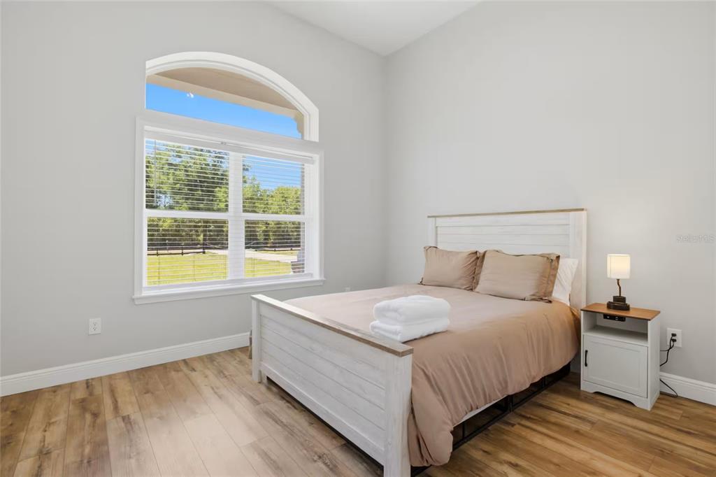 A bedroom with wood-look flooring, a white bed frame, and a large arched window — 9855 SW 125TH TERRACE, DUNNELLON, FL