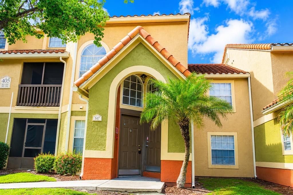 The exterior of a multi-story apartment building features a green arched entryway and palm tree — 405 FOUNTAINHEAD CIRCLE UNIT 247, KISSIMMEE, FL