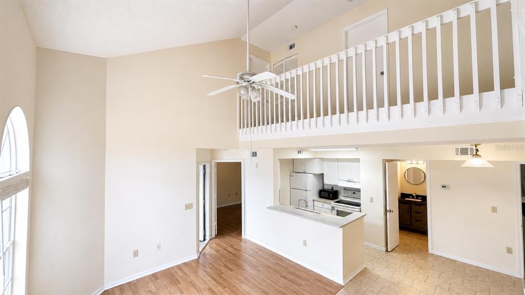 A high-ceilinged living area features a loft balcony, kitchen, and tile and wood flooring — 405 FOUNTAINHEAD CIRCLE UNIT 247, KISSIMMEE, FL