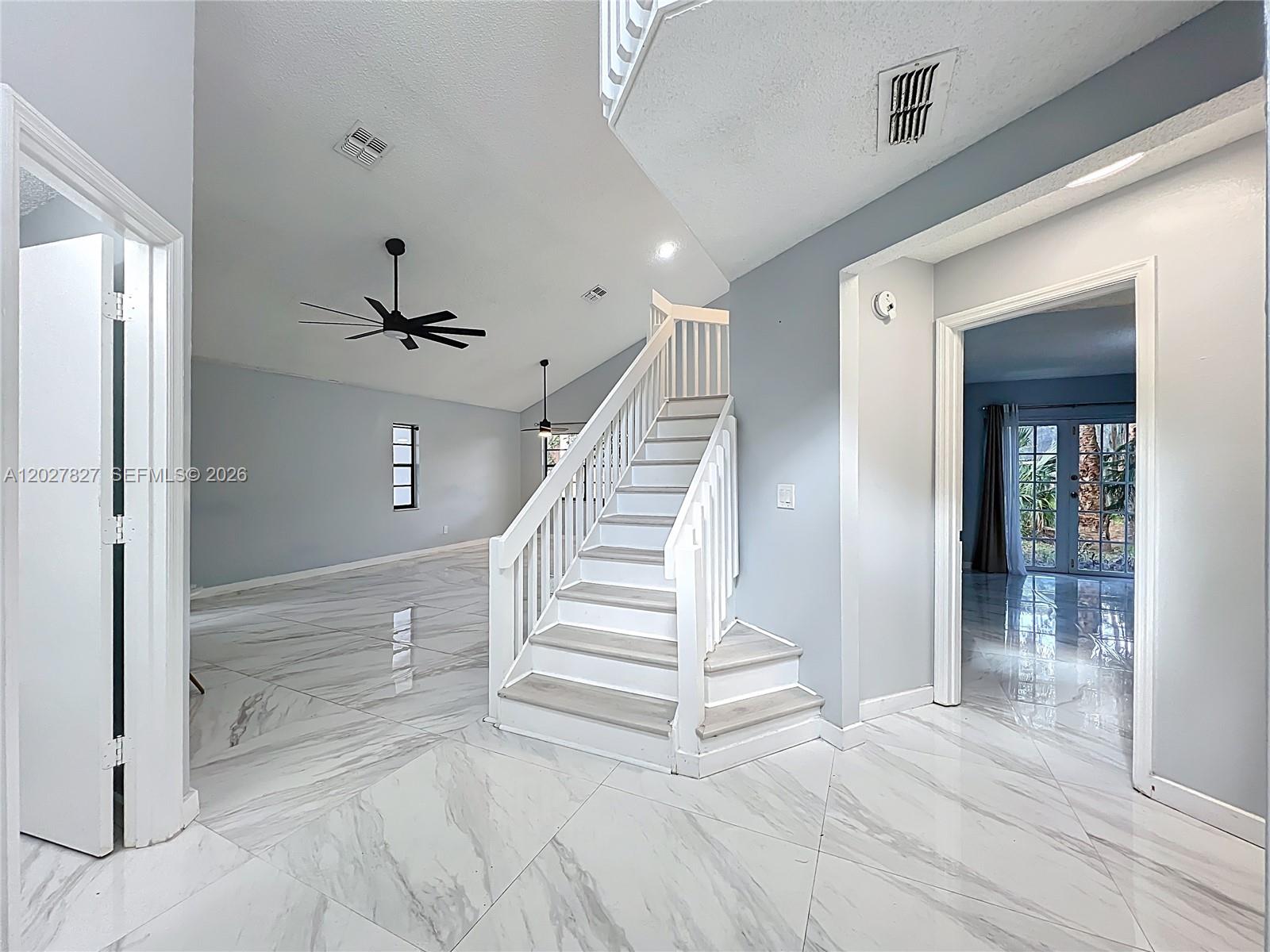 A bright room features a central staircase, light gray walls, and white marble-look tile flooring — OTHER CITY - IN THE STATE OF FLORIDA, FL