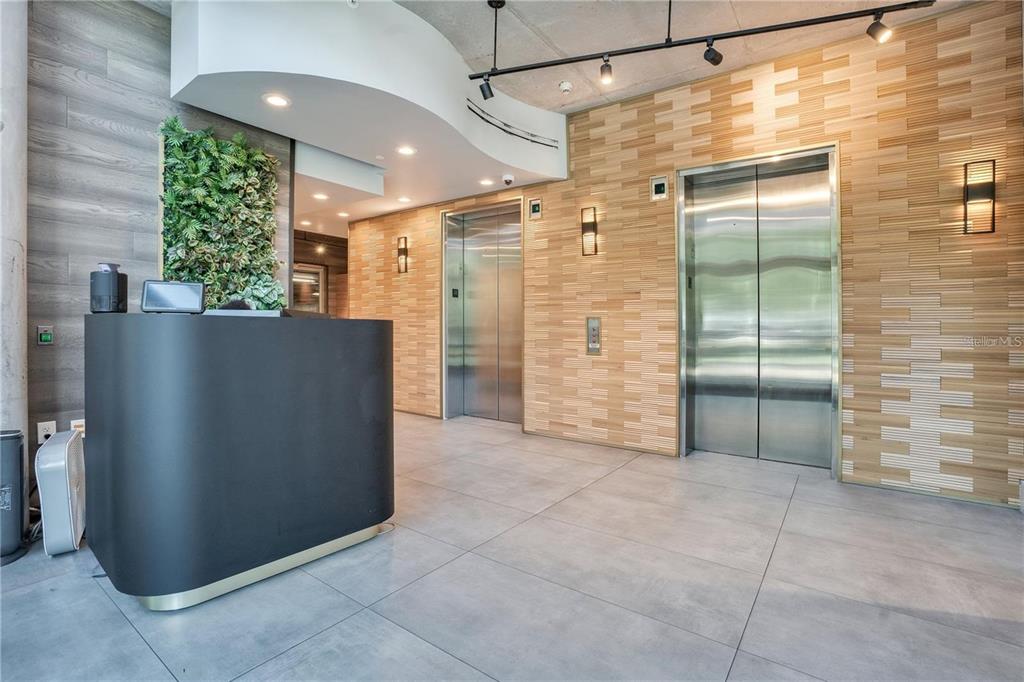 A modern lobby features a black reception desk, two stainless steel elevators, and wood-paneled walls — 525 E JACKSON STREET UNIT 403, ORLANDO, FL