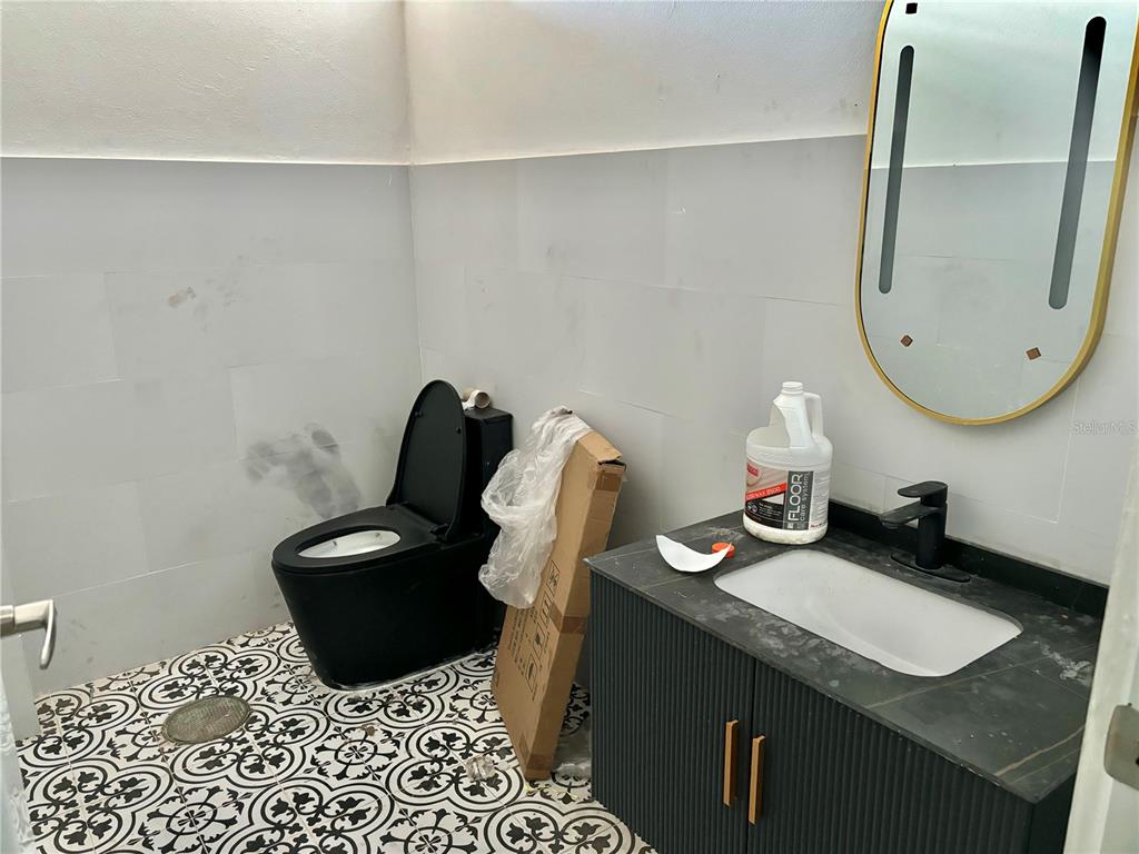 A bathroom features a black toilet, a vanity with a black sink, and patterned floor tiles — 20 LUIS MUNOZ RIVERA, AGUAS BUENAS, PR