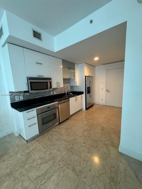 A modern kitchen features white cabinets, black countertops, stainless steel appliances, and marble flooring — 60 SW 13th St # 2210, Miami FL 33130, MIAMI, FL