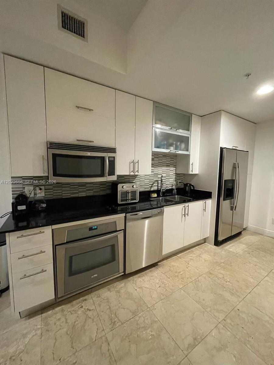 A modern kitchen features white cabinetry, stainless steel appliances, and dark granite countertops — 60 SW 13th St # 2210, Miami FL 33130, MIAMI, FL