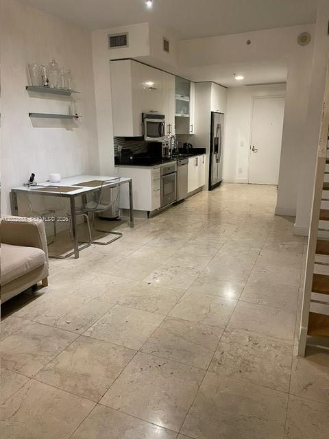 A modern kitchen with white cabinetry and a dining area with a glass table — 60 SW 13th St # 2210, Miami FL 33130, MIAMI, FL