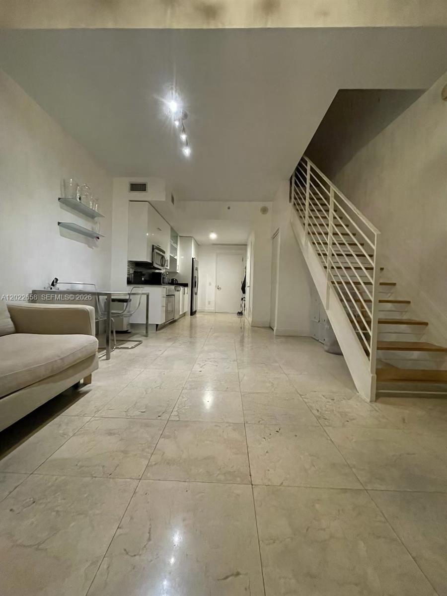 A living area with a sofa, dining table, kitchen, and a staircase with white railings — 60 SW 13th St # 2210, Miami FL 33130, MIAMI, FL
