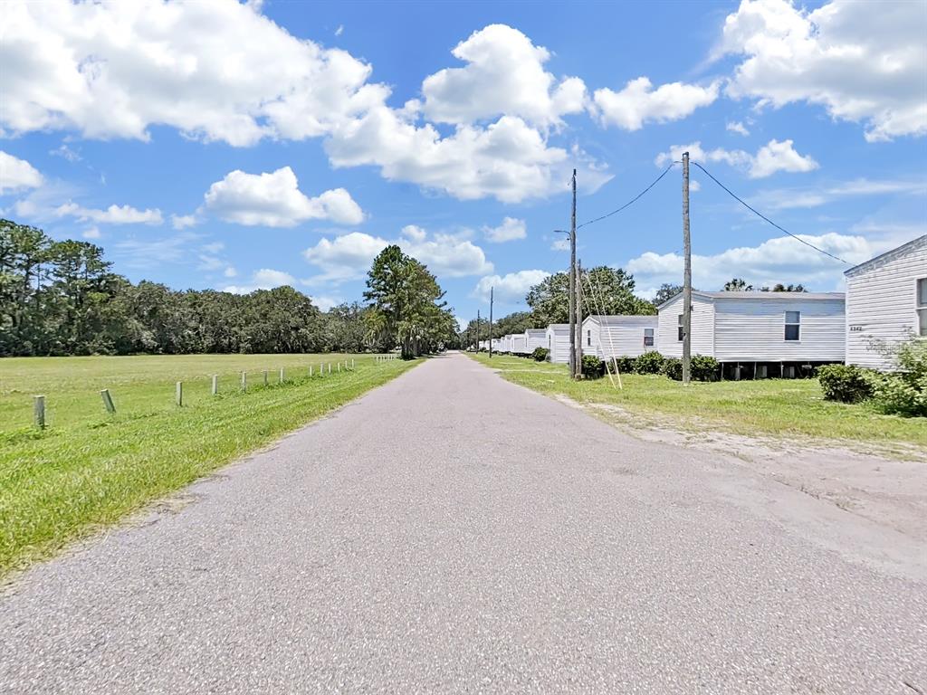 A paved road runs between a grassy field and a row of white mobile homes — 6330 EUGENE ACRES LANE, GIBSONTON, FL