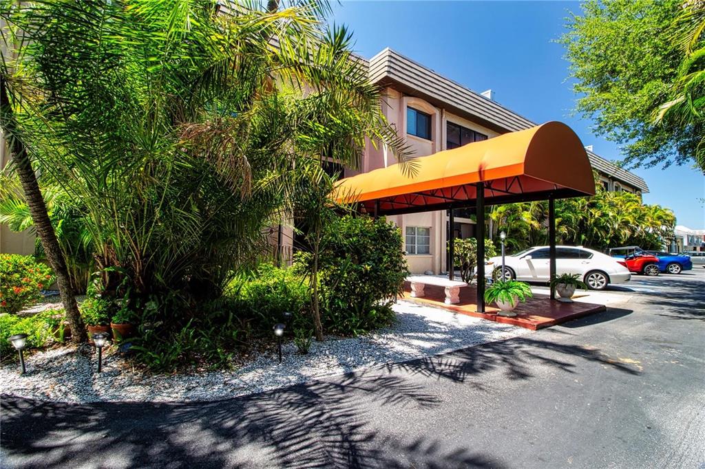 An orange awning covers the entrance to a multi-story building with palm trees and parking — 3700 S OSPREY AVENUE UNIT 216, SARASOTA, FL