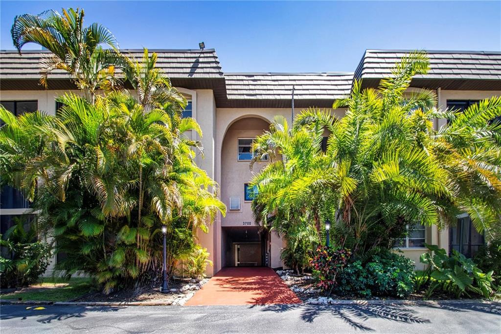 An exterior view of a multi-story apartment building entrance flanked by large palm trees — 3700 S OSPREY AVENUE UNIT 216, SARASOTA, FL