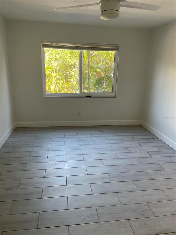 An empty bedroom features light gray wood-look tile flooring, white walls, and a ceiling fan — 3700 S OSPREY AVENUE UNIT 216, SARASOTA, FL