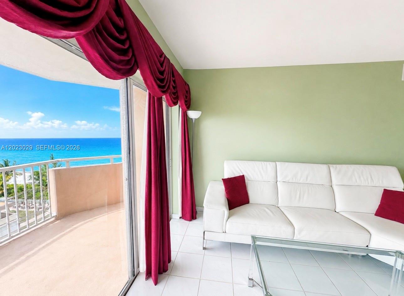 A living room features a white leather sofa, green walls, and a balcony overlooking the ocean — 1950 S Ocean Dr # 8K, Hallandale Beach FL 33009, HALLANDALE BEACH, FL