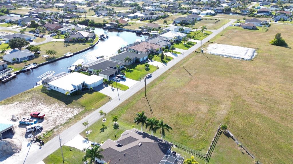 An aerial view shows a suburban neighborhood with houses, a canal, and vacant lots — 3405 NW 6TH STREET, CAPE CORAL, FL