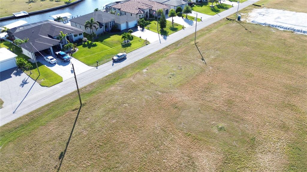 An aerial view shows a vacant grassy lot adjacent to a paved road and houses — 3405 NW 6TH STREET, CAPE CORAL, FL