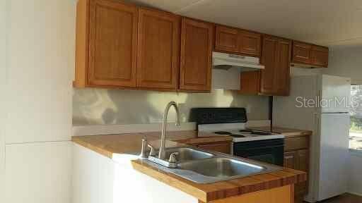 A kitchen features wood cabinets, a double sink, a stove, and a white refrigerator — 3366 MAPLE LANE, HAINES CITY, FL