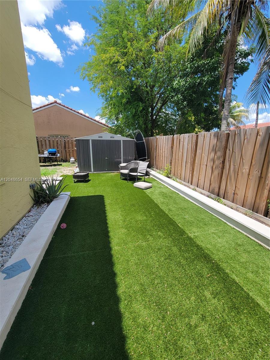 A narrow backyard features artificial turf, a storage shed, and a wooden privacy fence — 6606 Saltaire Ter, Margate FL 33063, MARGATE, FL