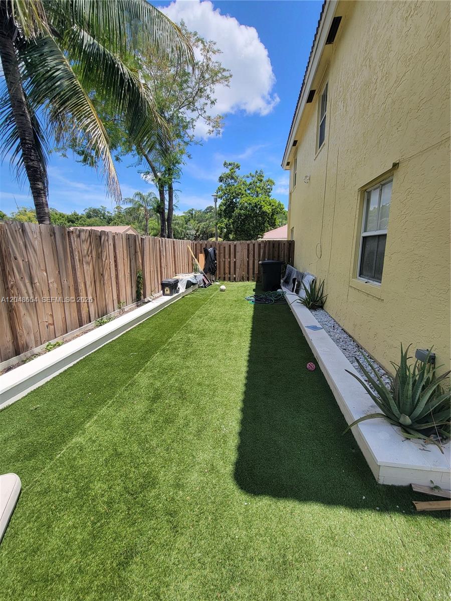 A narrow backyard features artificial turf, a wooden fence, and a raised concrete planter bed — 6606 Saltaire Ter, Margate FL 33063, MARGATE, FL