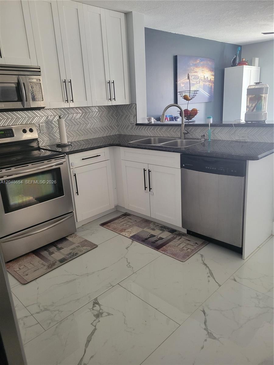 A kitchen features white cabinets, stainless steel appliances, dark countertops, and a herringbone backsplash — 6606 Saltaire Ter, Margate FL 33063, MARGATE, FL
