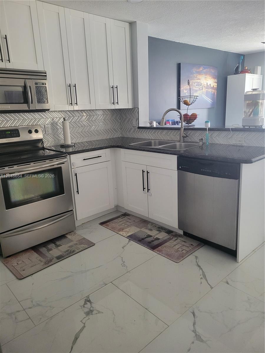A kitchen features white cabinets, stainless steel appliances, dark countertops, and a herringbone tile backsplash — 6606 Saltaire Ter, Margate FL 33063, MARGATE, FL