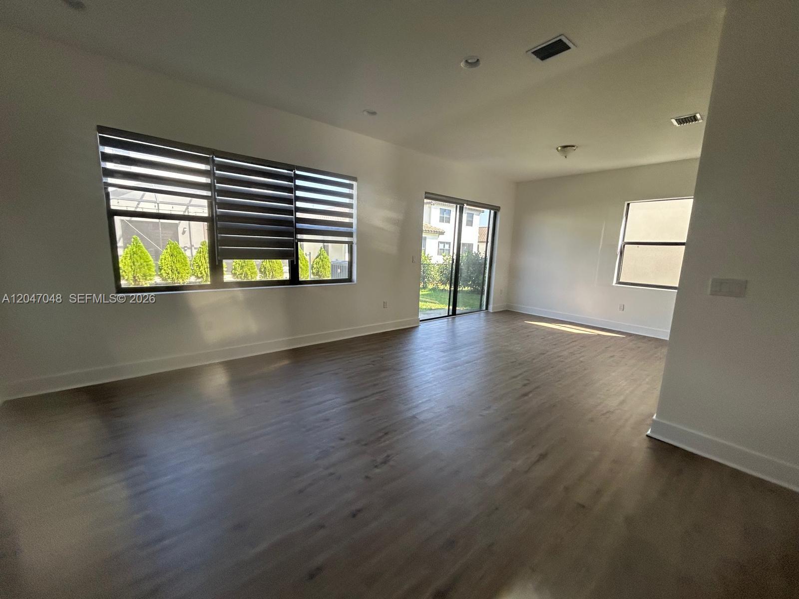 An empty room features light wood-look flooring, white walls, large windows, and sliding glass doors — 5525 AGOSTINO WAY, Ave Maria FL 34142, AVE MARIA, FL