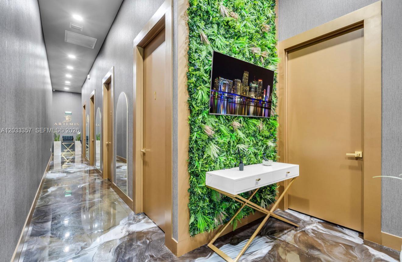 A hallway features a green wall with a television, a white console table, and doors — MIAMI, FL
