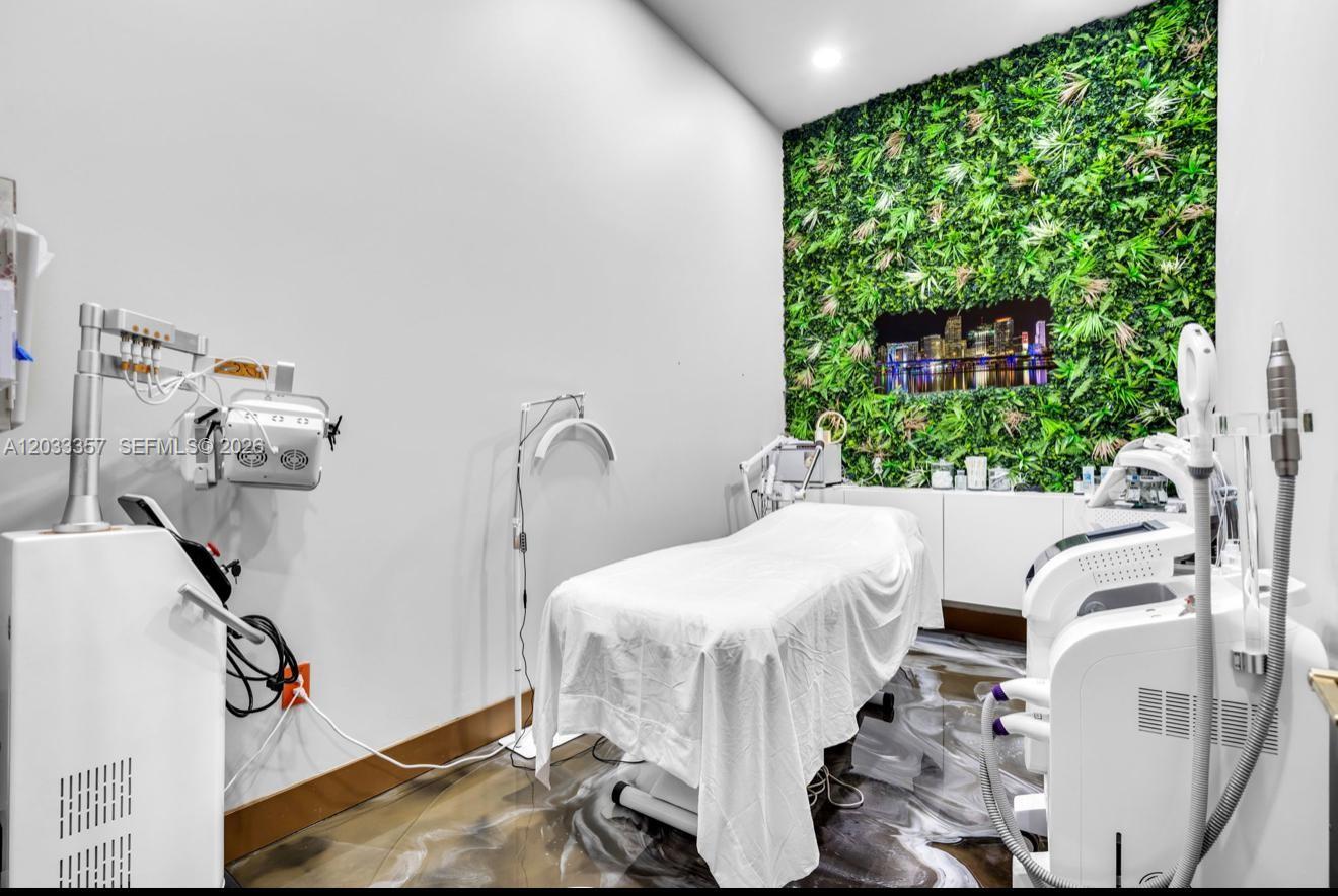 A treatment room features a massage table, medical equipment, and a green wall backdrop — MIAMI, FL