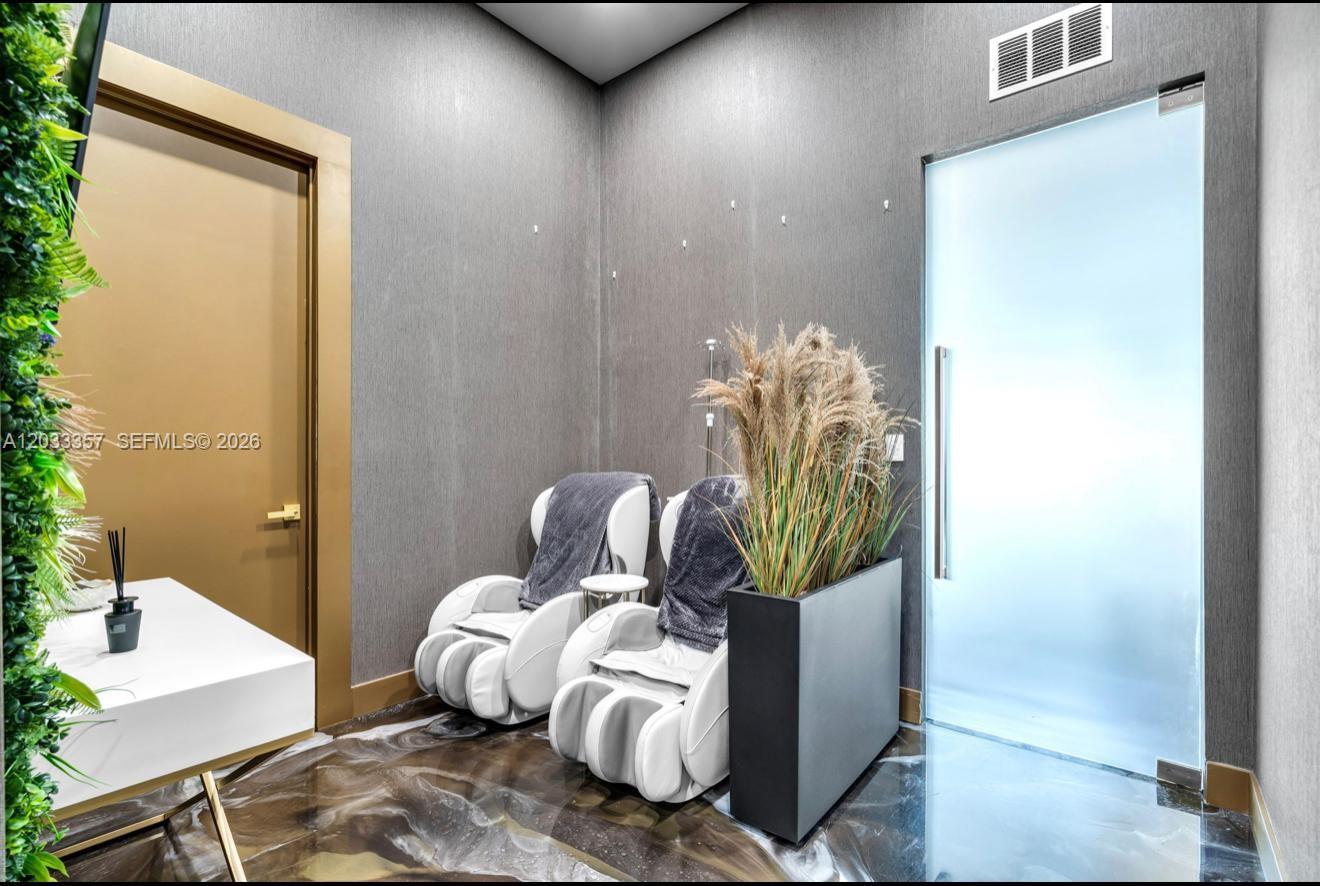 A modern room features two white massage chairs, a tall planter, and a glass door — MIAMI, FL